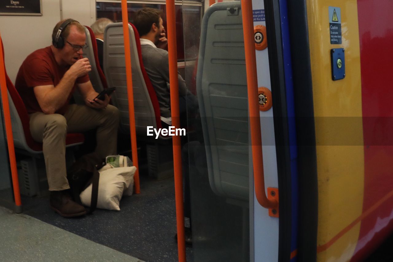 REAR VIEW OF MAN SITTING ON TRAIN