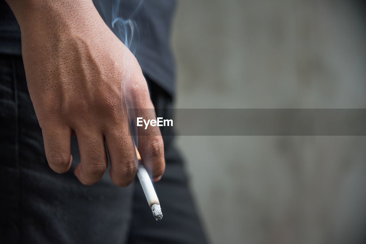 Midsection of man holding cigarette