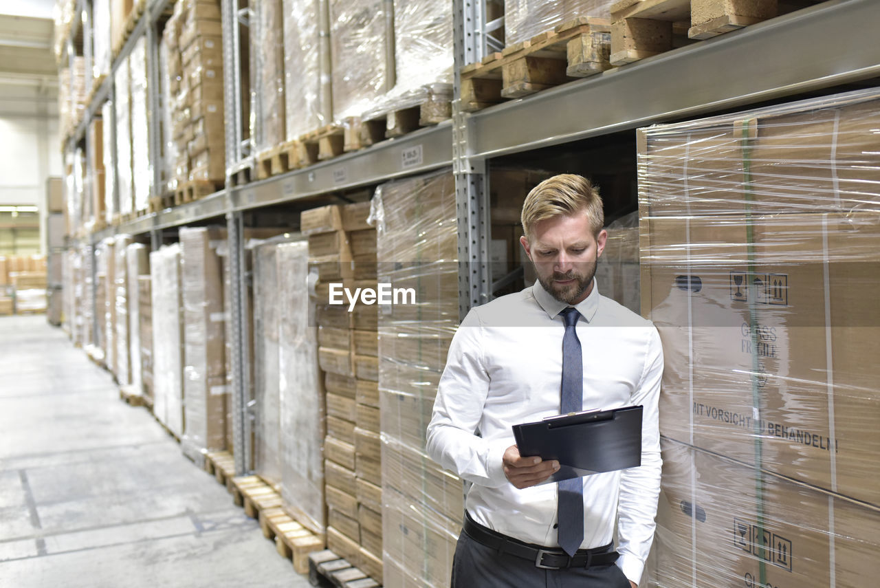 Businessman looking at clipboard in warehouse