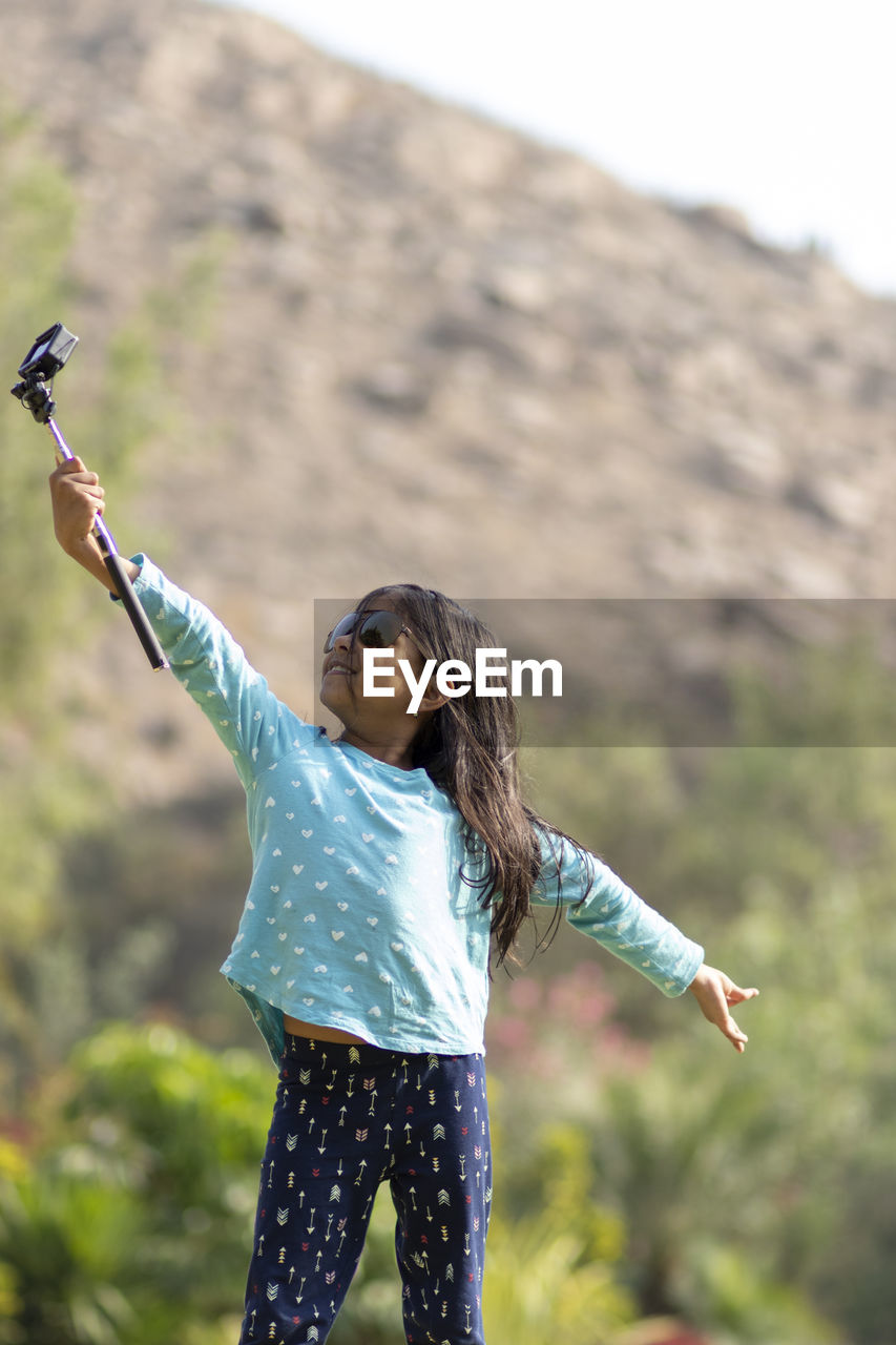 YOUNG WOMAN WITH ARMS OUTSTRETCHED STANDING ON ROCK