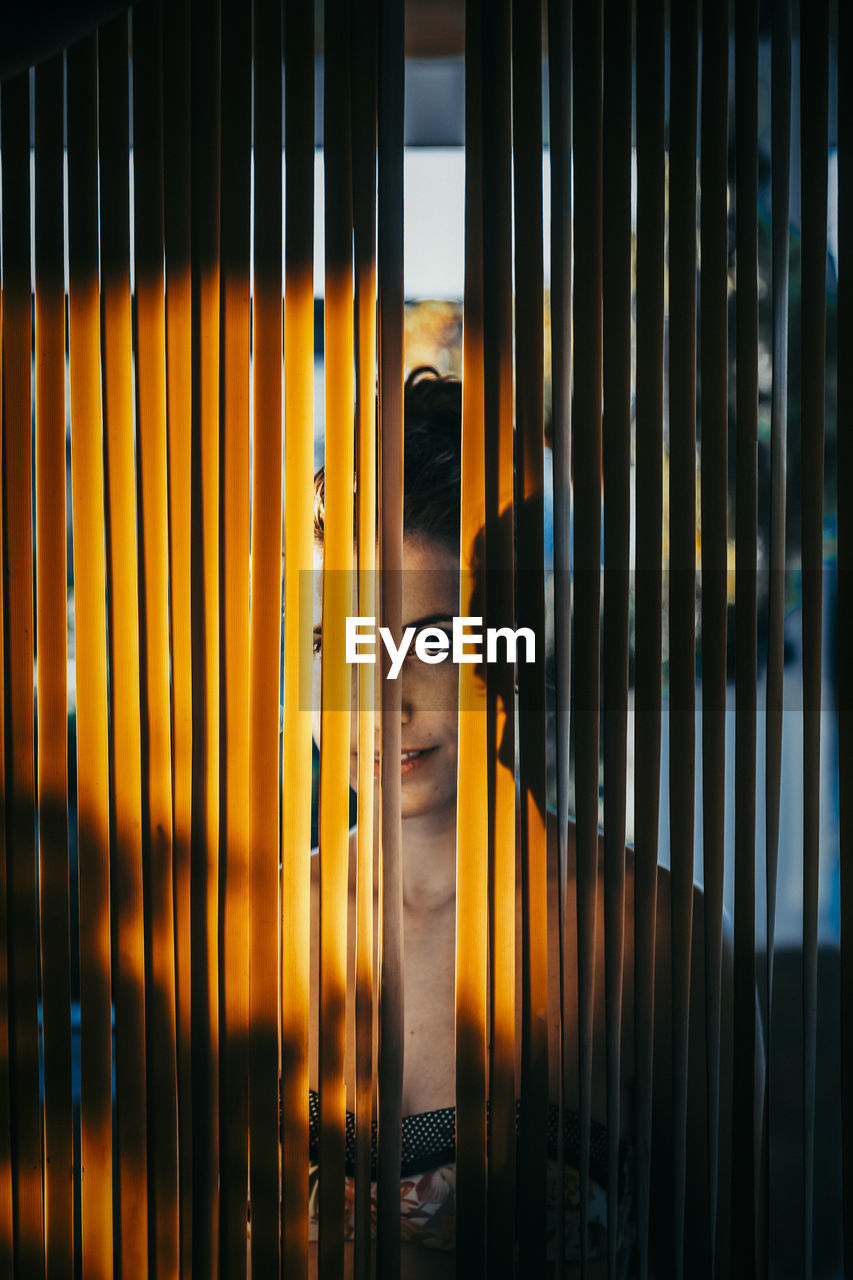 Close-up portrait of woman looking through window blinds