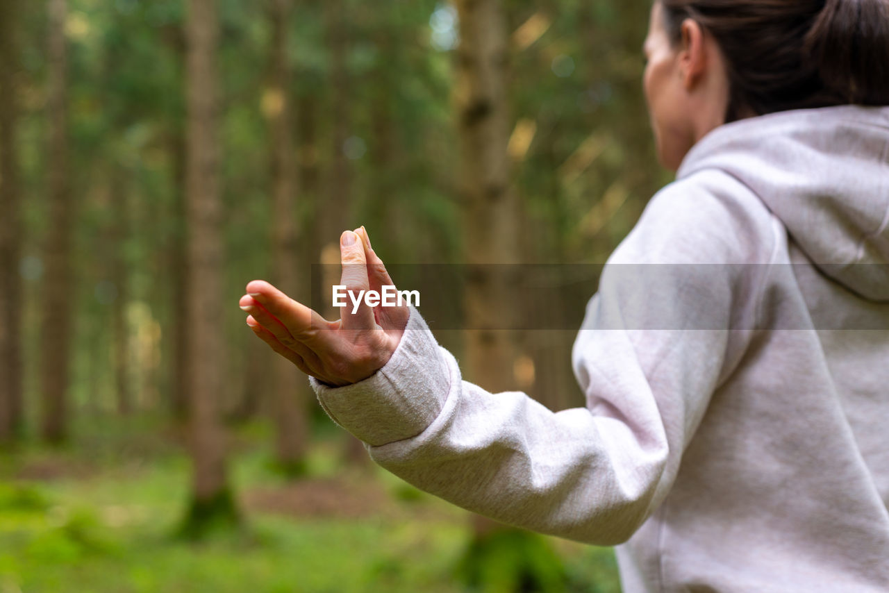 Cropped unrecognizable female traveler sitting on tree stump in lotus pose and doing yoga with closed eyes while enjoying woods