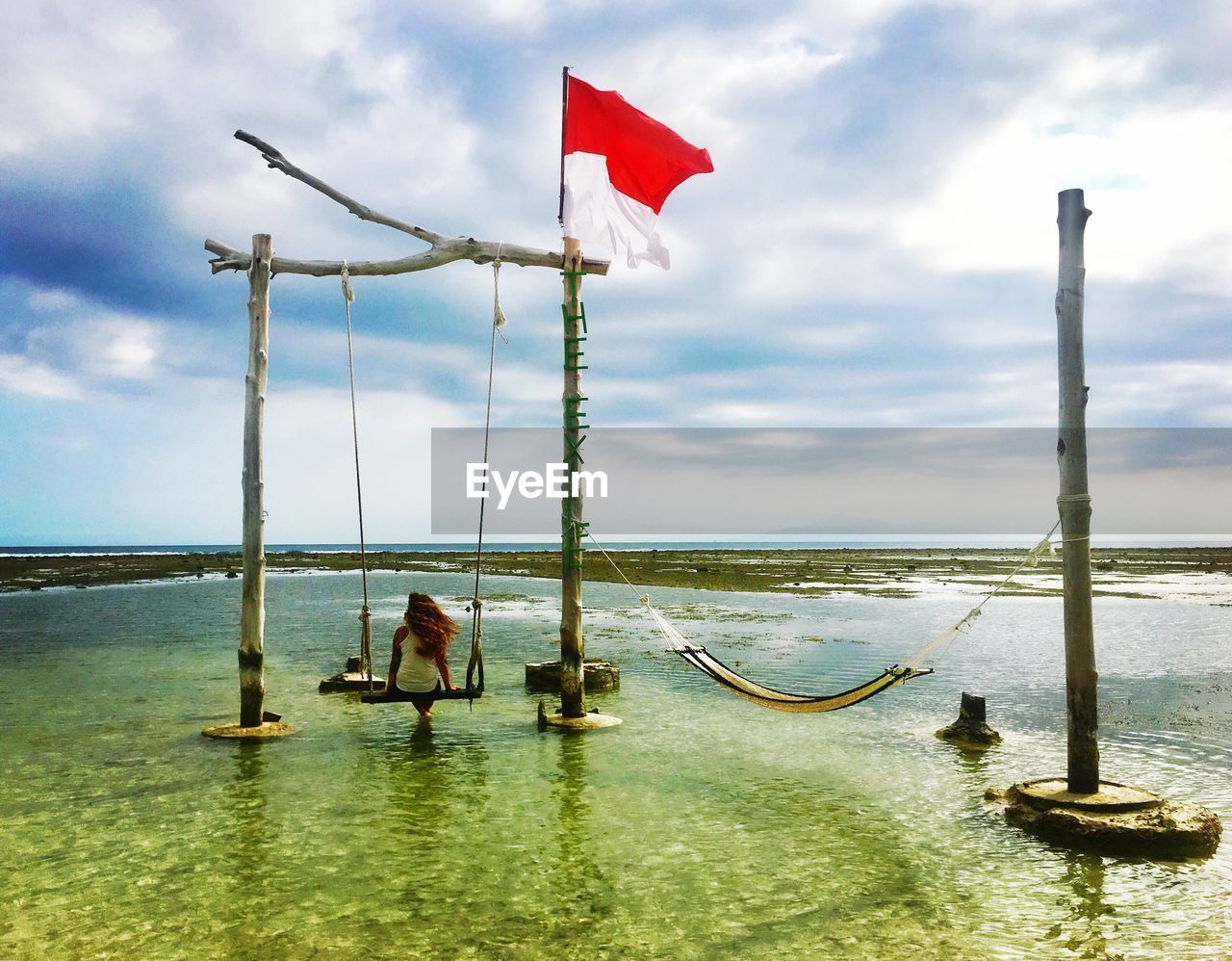 Rear view of woman sitting on swing in sea against sky