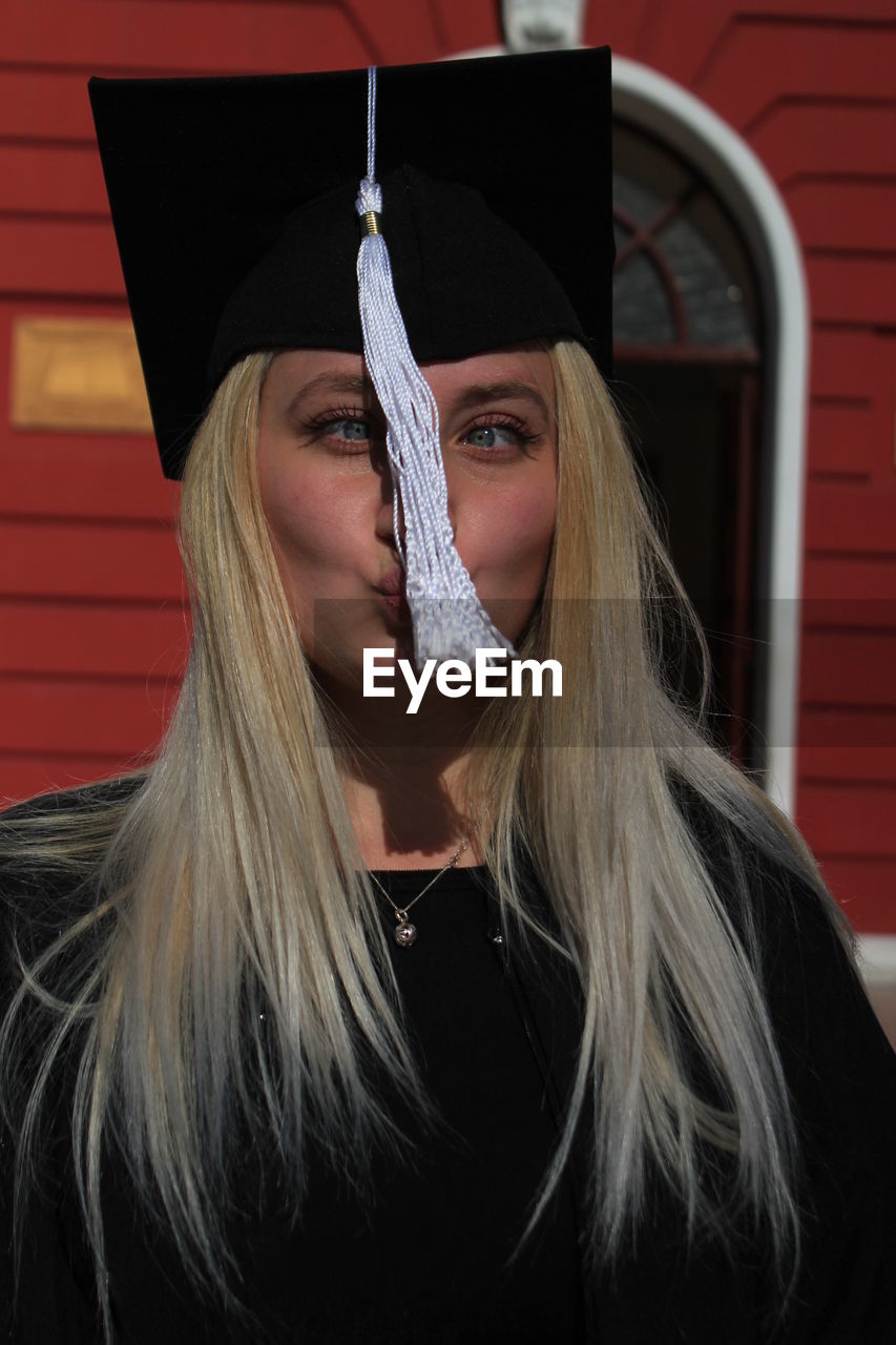 Playful young woman making face while wearing mortarboard