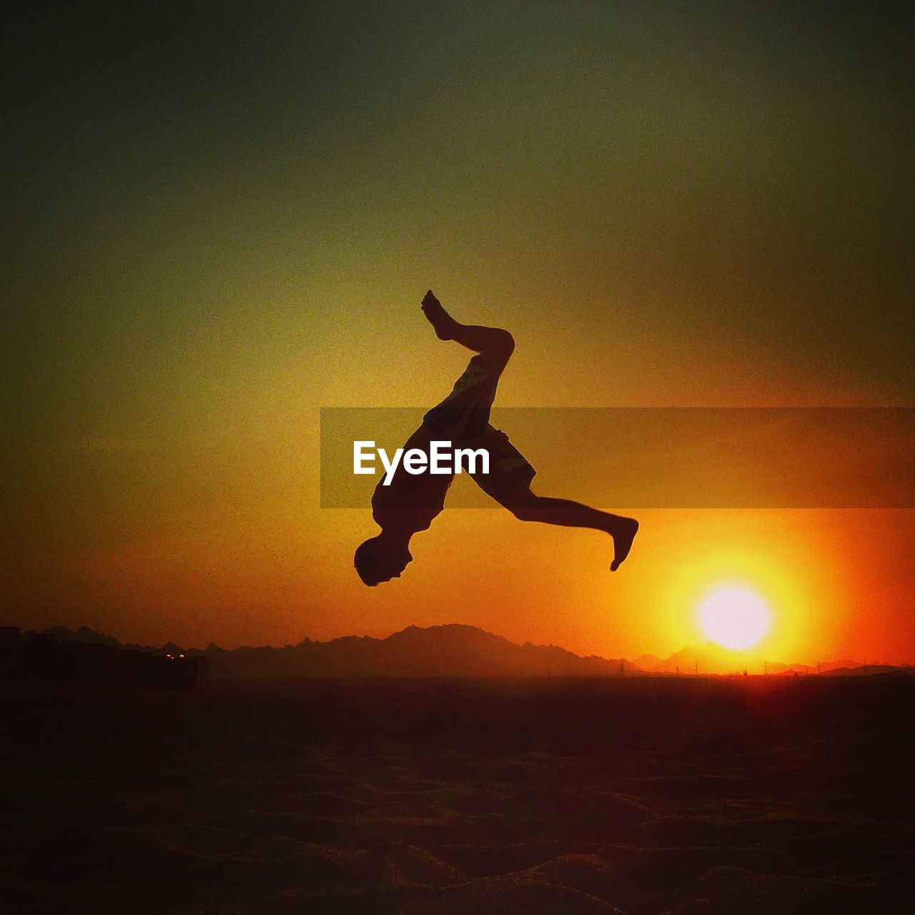 FULL LENGTH OF MAN JUMPING IN MID-AIR DURING SUNSET