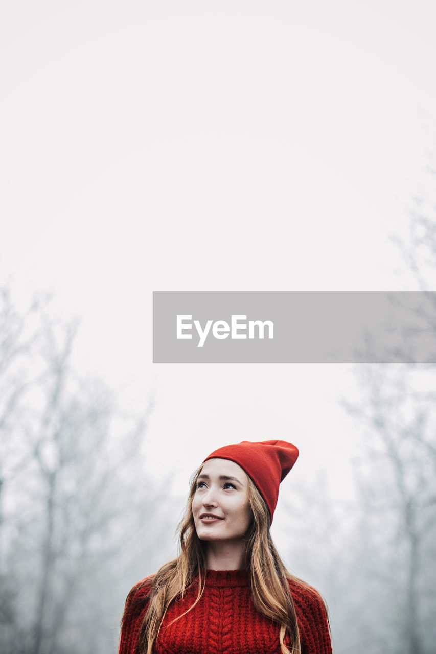 Woman in red hat and sweater walking on foggy mystical morning forest.