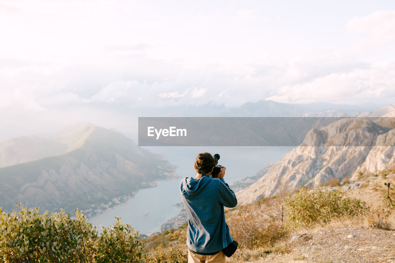 REAR VIEW OF MAN LOOKING AT MOUNTAIN