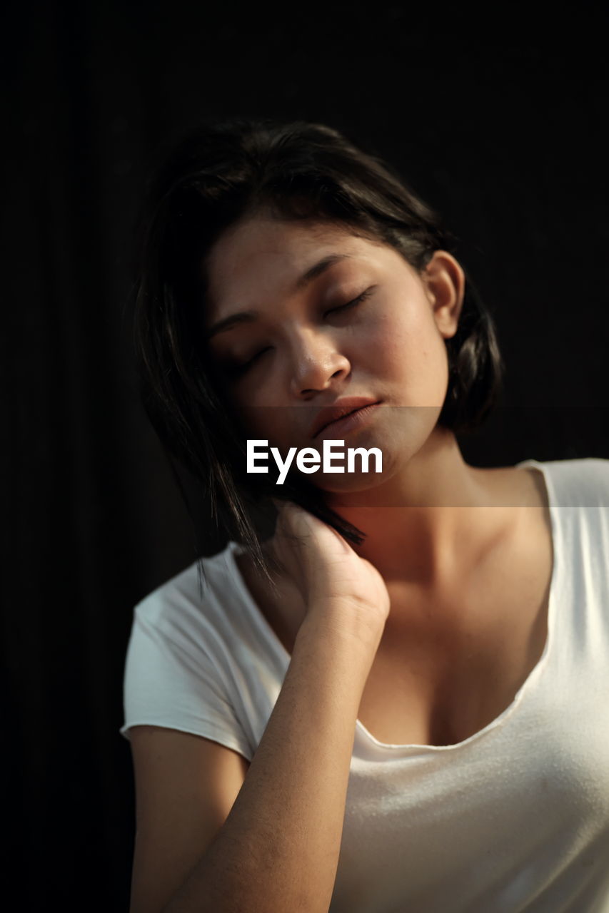 Close-up of young woman against black background