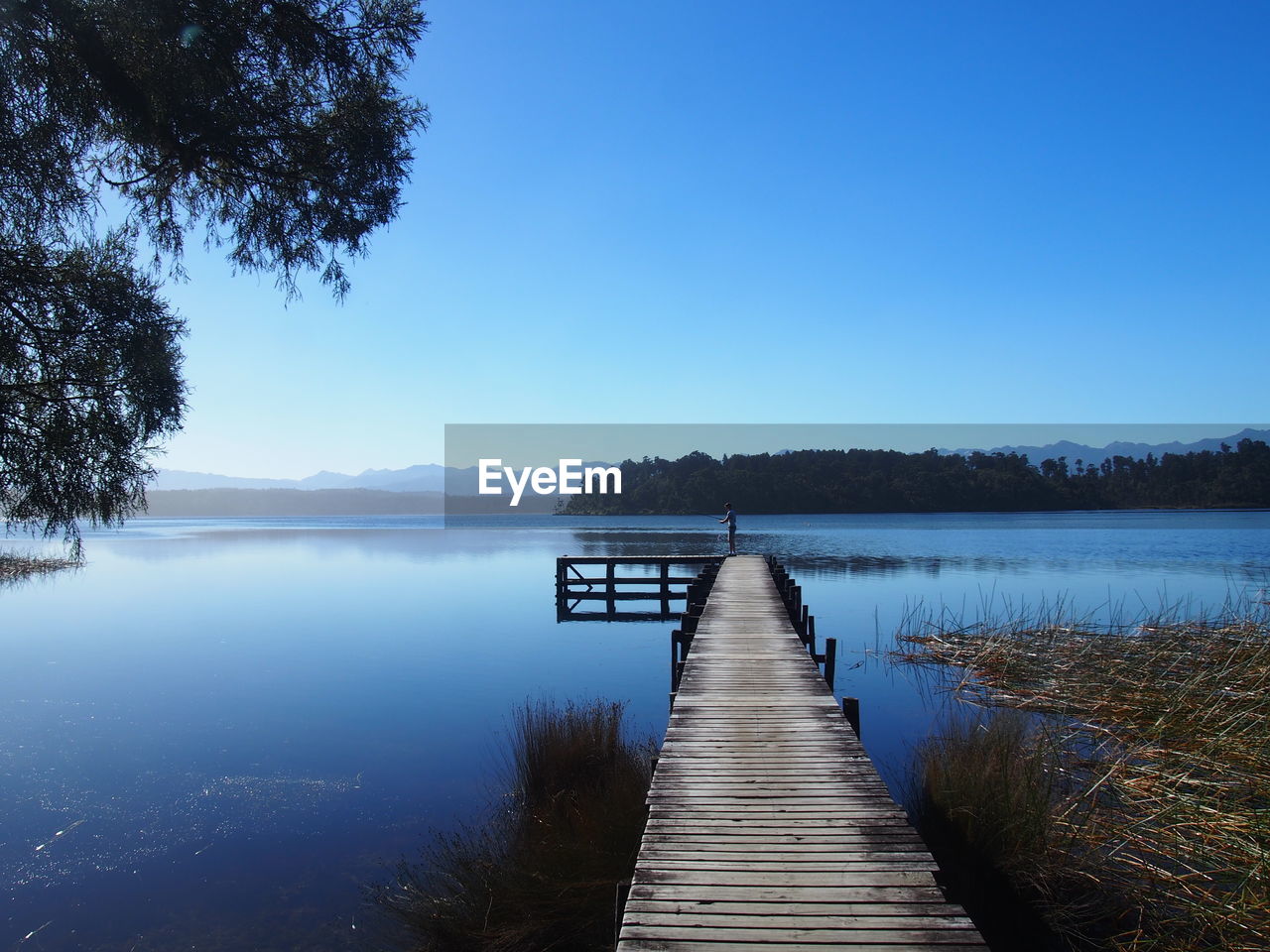 Pier over lake against clear blue sky