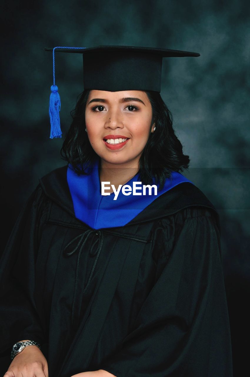 Portrait of smiling young woman in graduation gown against colored background