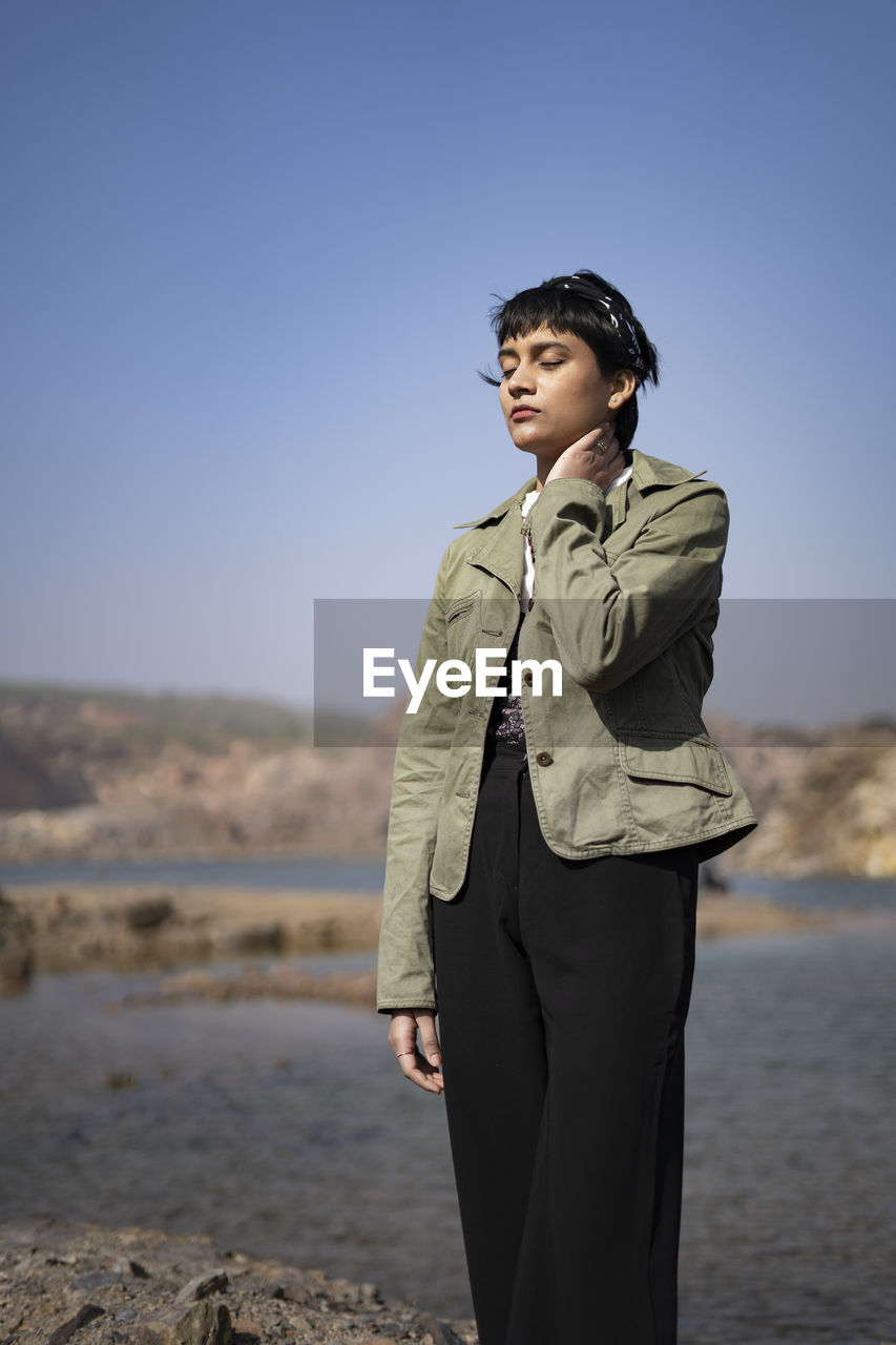 A young beautiful indian girl standing neat a lake in the mountains with a hand on her neck