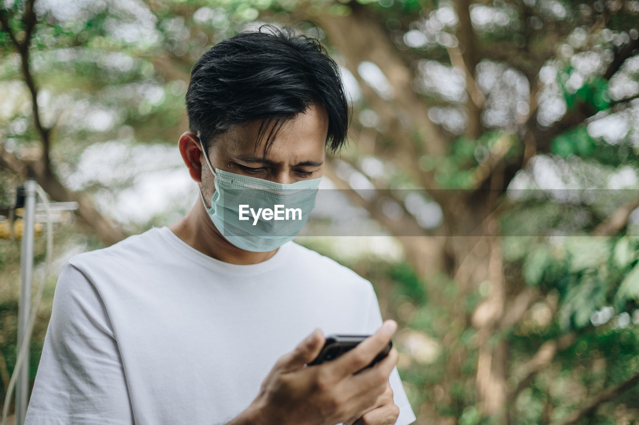 Man using mobile phone while wearing mask against trees