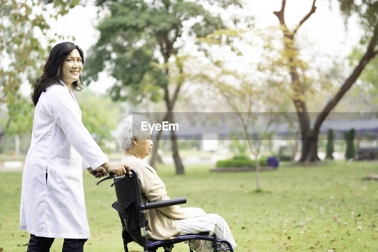 Portrait of nurse pushing senior woman sitting on wheelchair in park