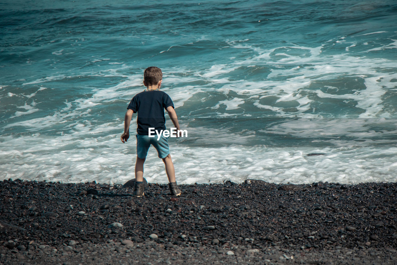 REAR VIEW OF MAN LOOKING AT SEA SHORE