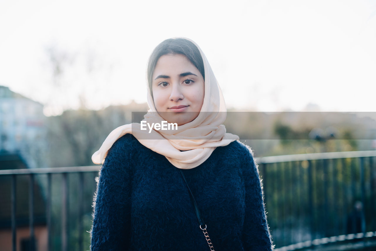 Portrait of confident teenage girl wearing hijab looking away against sky