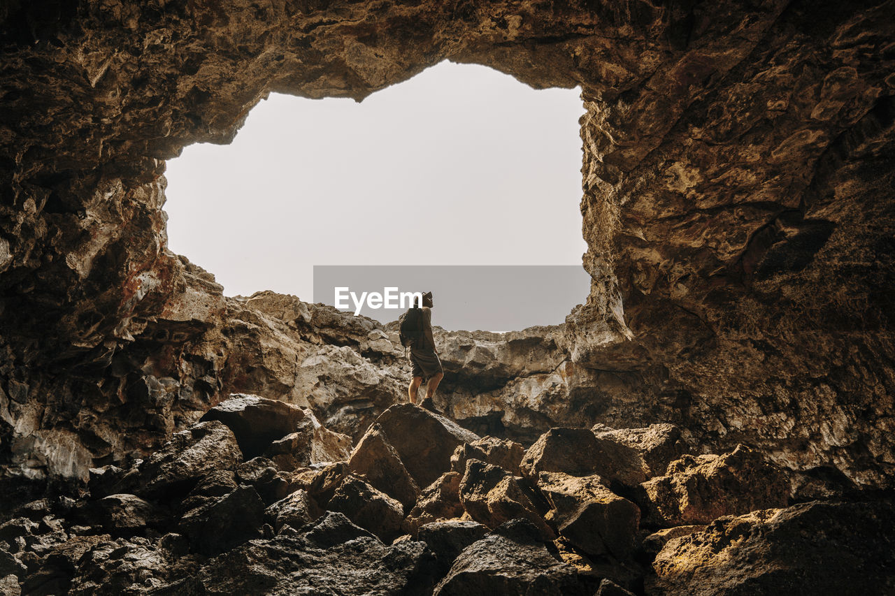 Low angle view of man spelunking cave against clear sky