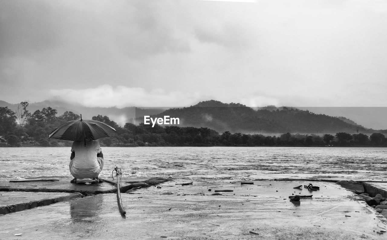 Rear view of woman by lake against sky