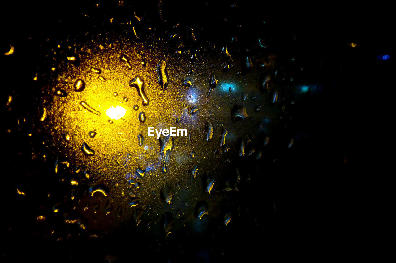 CLOSE-UP OF WET WINDOW IN ILLUMINATED NIGHT