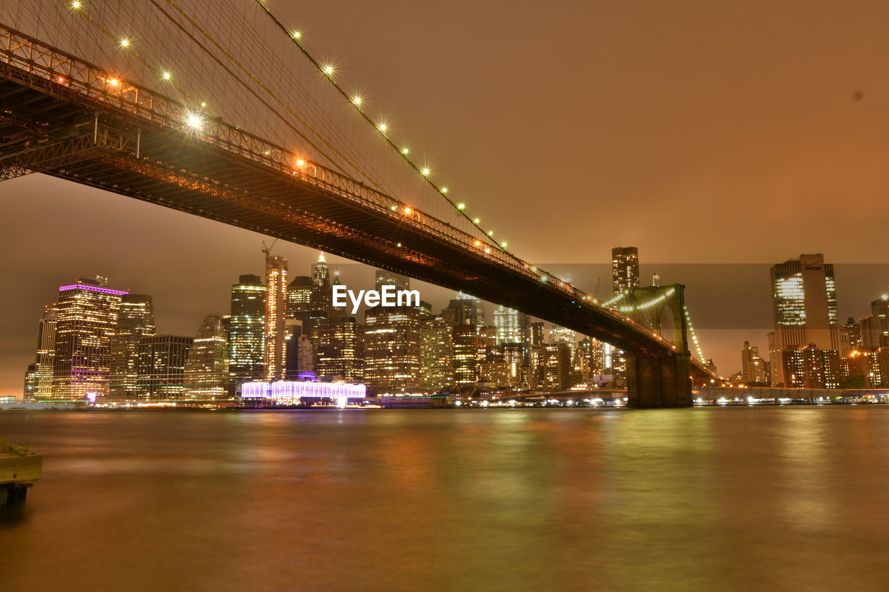 ILLUMINATED SUSPENSION BRIDGE OVER RIVER AT NIGHT