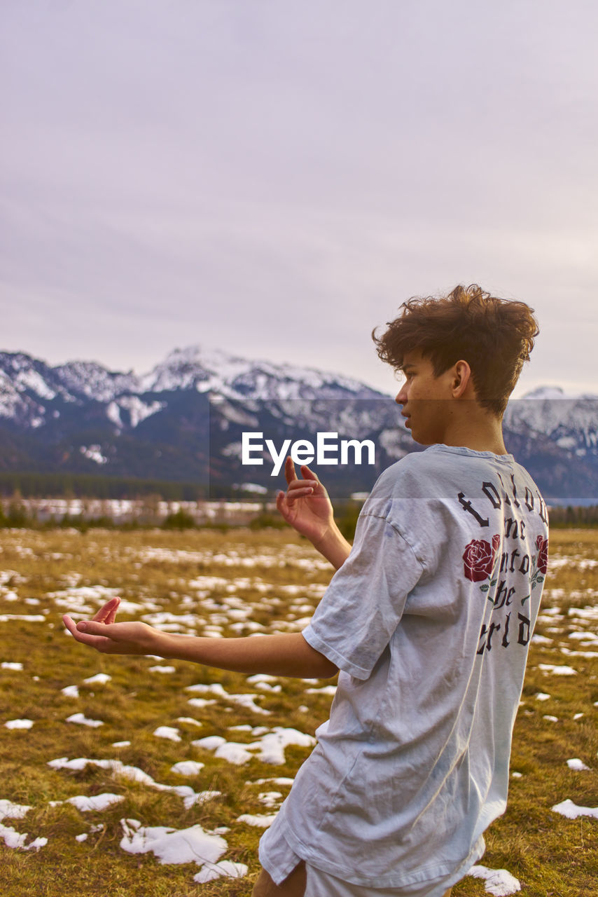 Young man gesturing while standing on field against mountain during winter