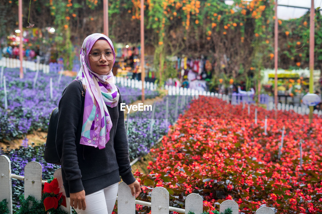 Portrait of smiling young woman standing by purple flowering plants