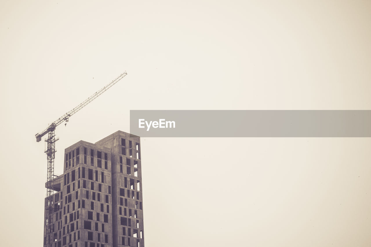 Low angle view of crane by building against clear sky