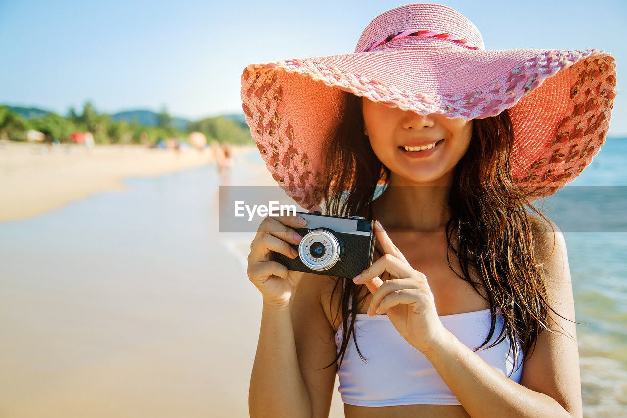 Young woman in hat against sky on beach