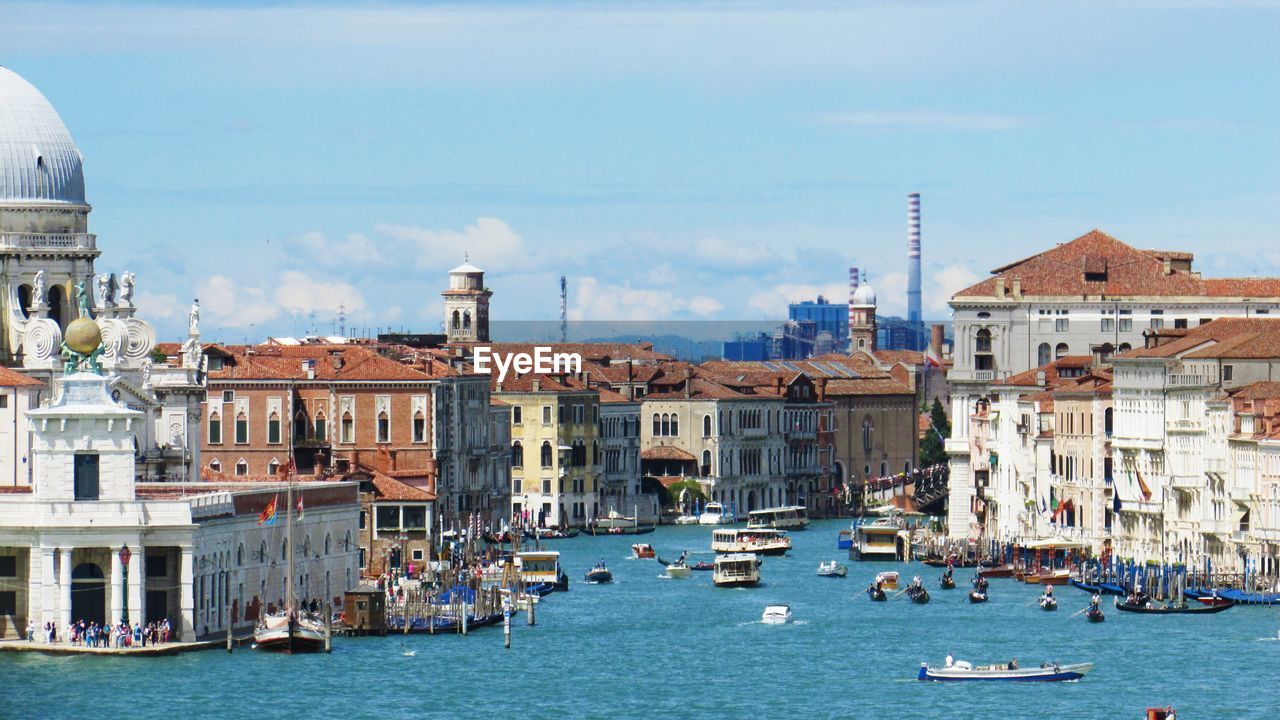 Boats in canal amidst buildings in city against sky