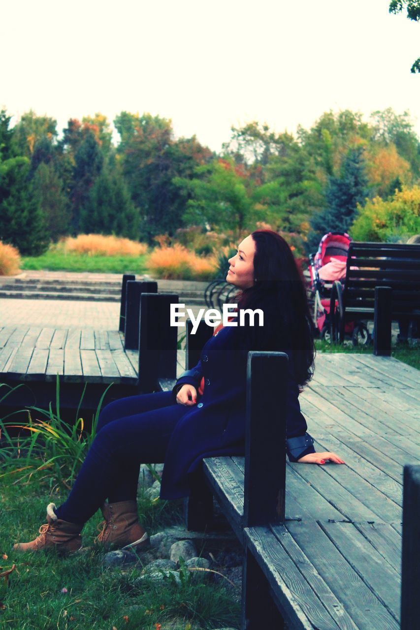 YOUNG WOMAN USING MOBILE PHONE WHILE SITTING ON BENCH