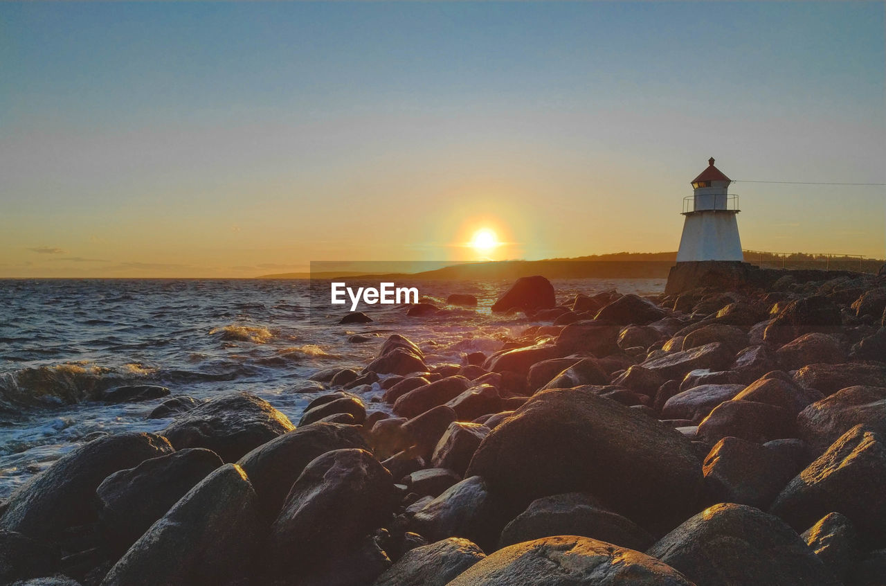 LIGHTHOUSE BY SEA AGAINST SKY AT SUNSET