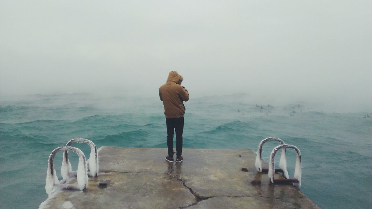 Rear view full length of man standing on pier by sea during foggy weather