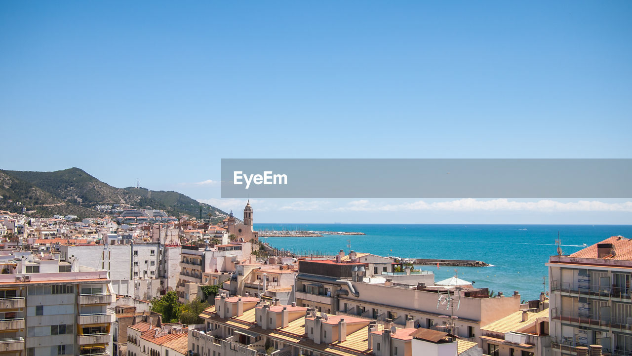 HIGH ANGLE VIEW OF BUILDINGS BY SEA AGAINST BLUE SKY