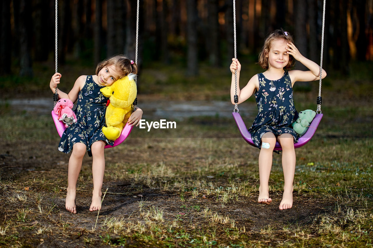 Portrait of cute girls sitting on swing at park