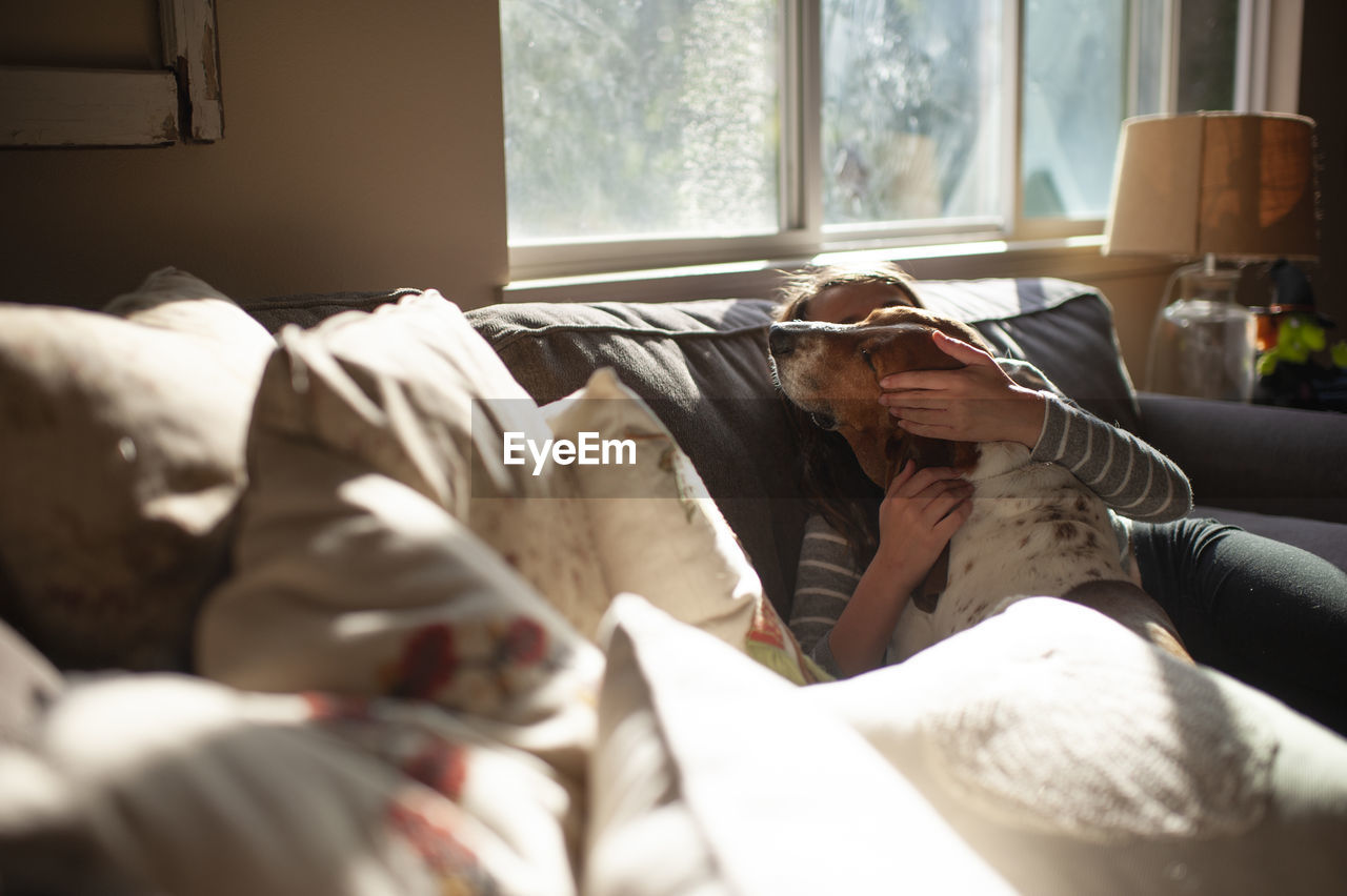 Girl hugging and kissing her dog on couch at home in pretty light