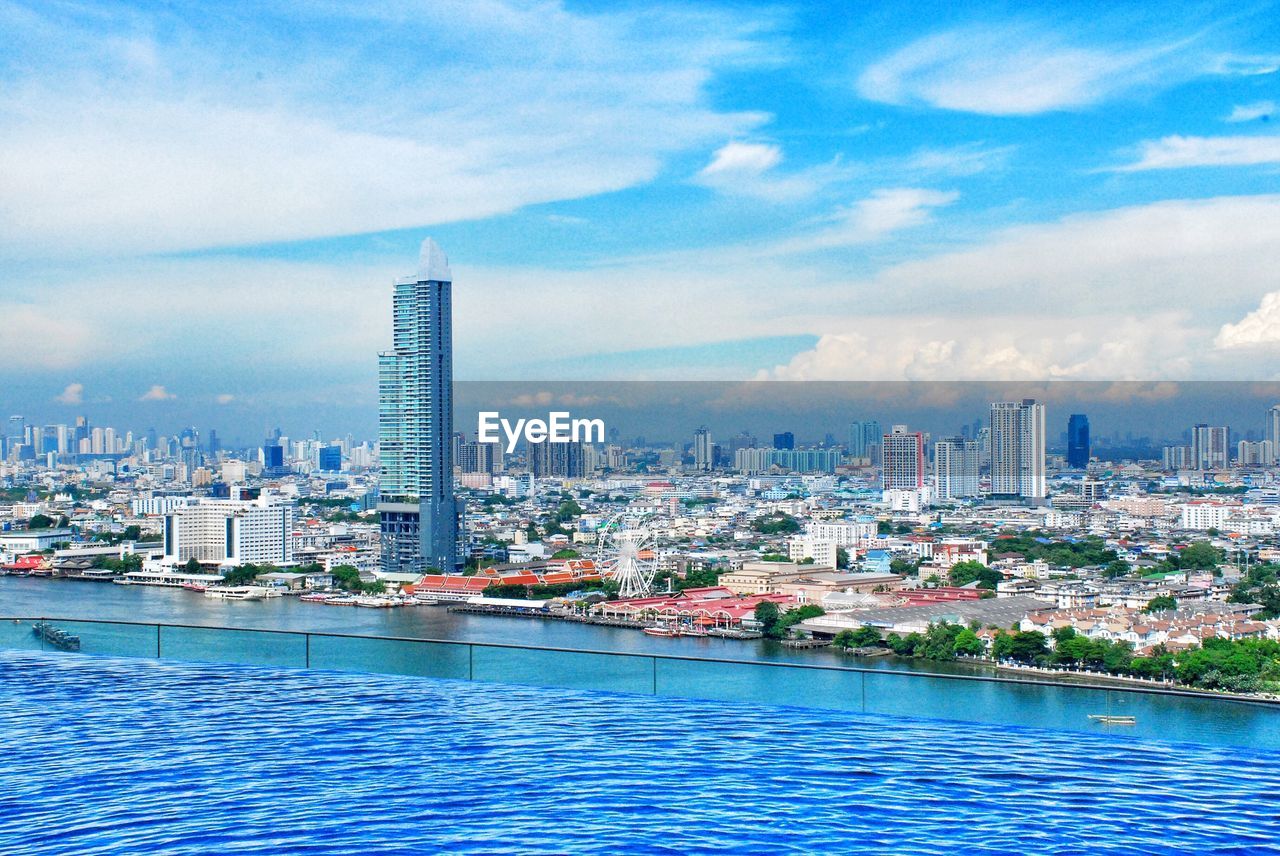 VIEW OF SWIMMING POOL BY BUILDINGS AGAINST SKY IN CITY