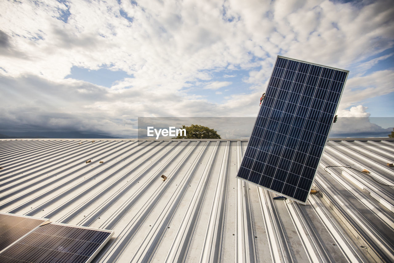 Low angle of hidden person carrying solar panel on roof.