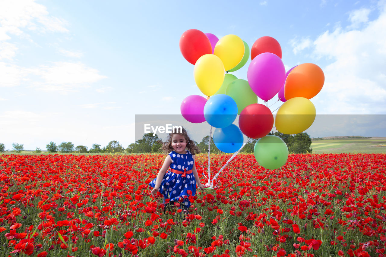 Girl holding colorful balloons while standing on field against sky