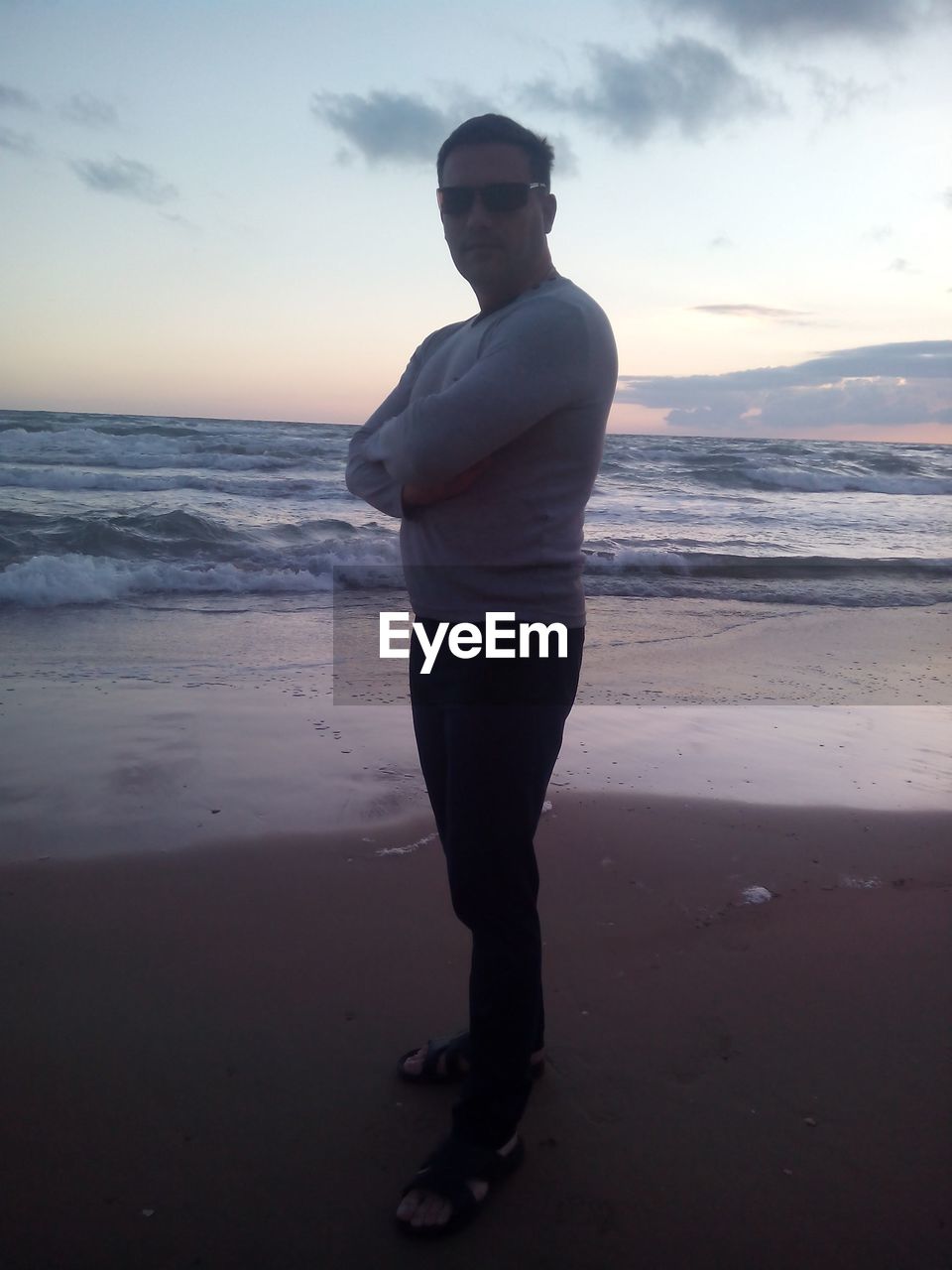 MAN STANDING ON BEACH AGAINST SKY DURING SUNSET