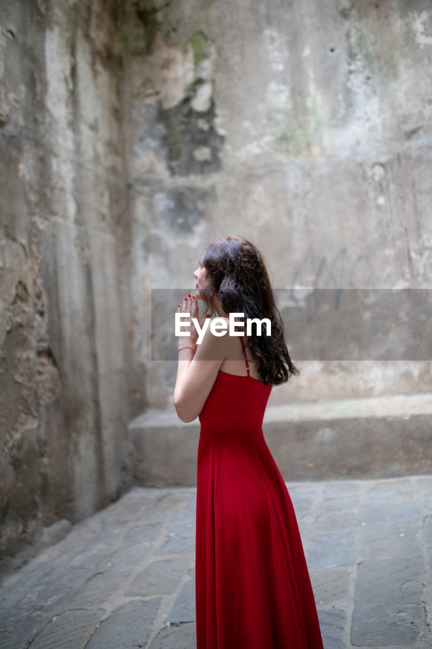 Side view of woman praying while standing against wall