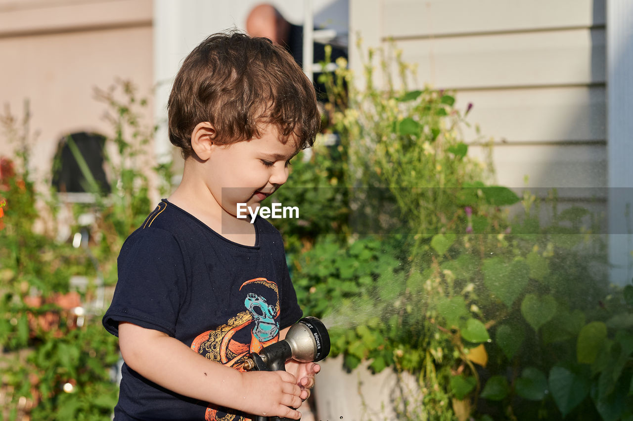 Little boy playing with a watering hose in the backyard