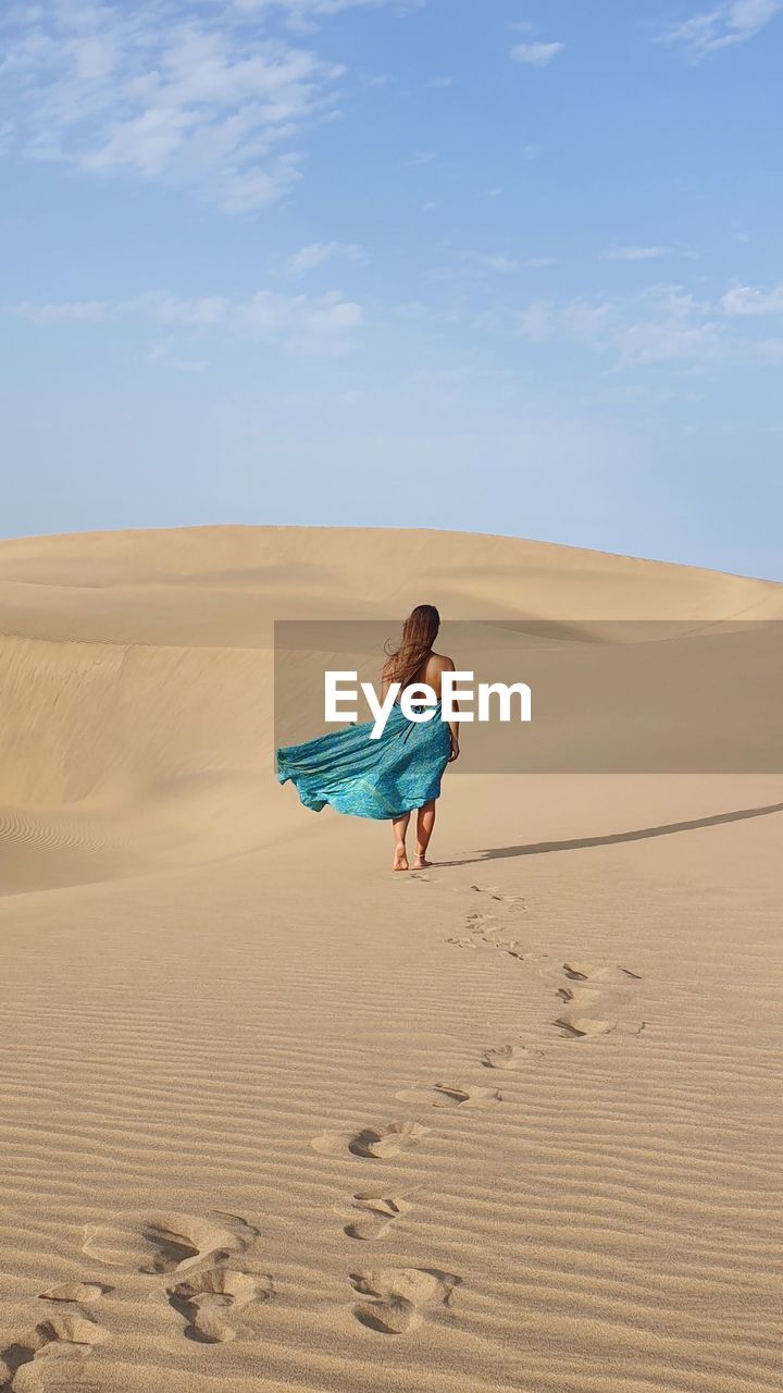 Woman with long dress on sand dune in desert against sky