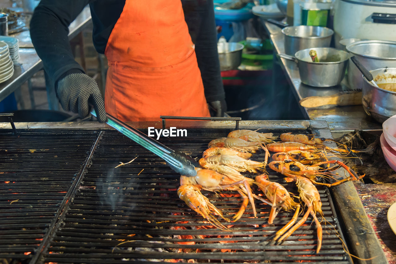 Midsection of man preparing shrimps on barbecue