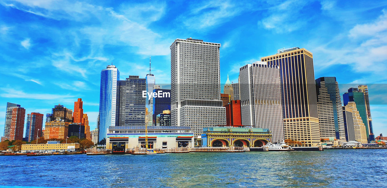 MODERN BUILDINGS BY RIVER AGAINST SKY