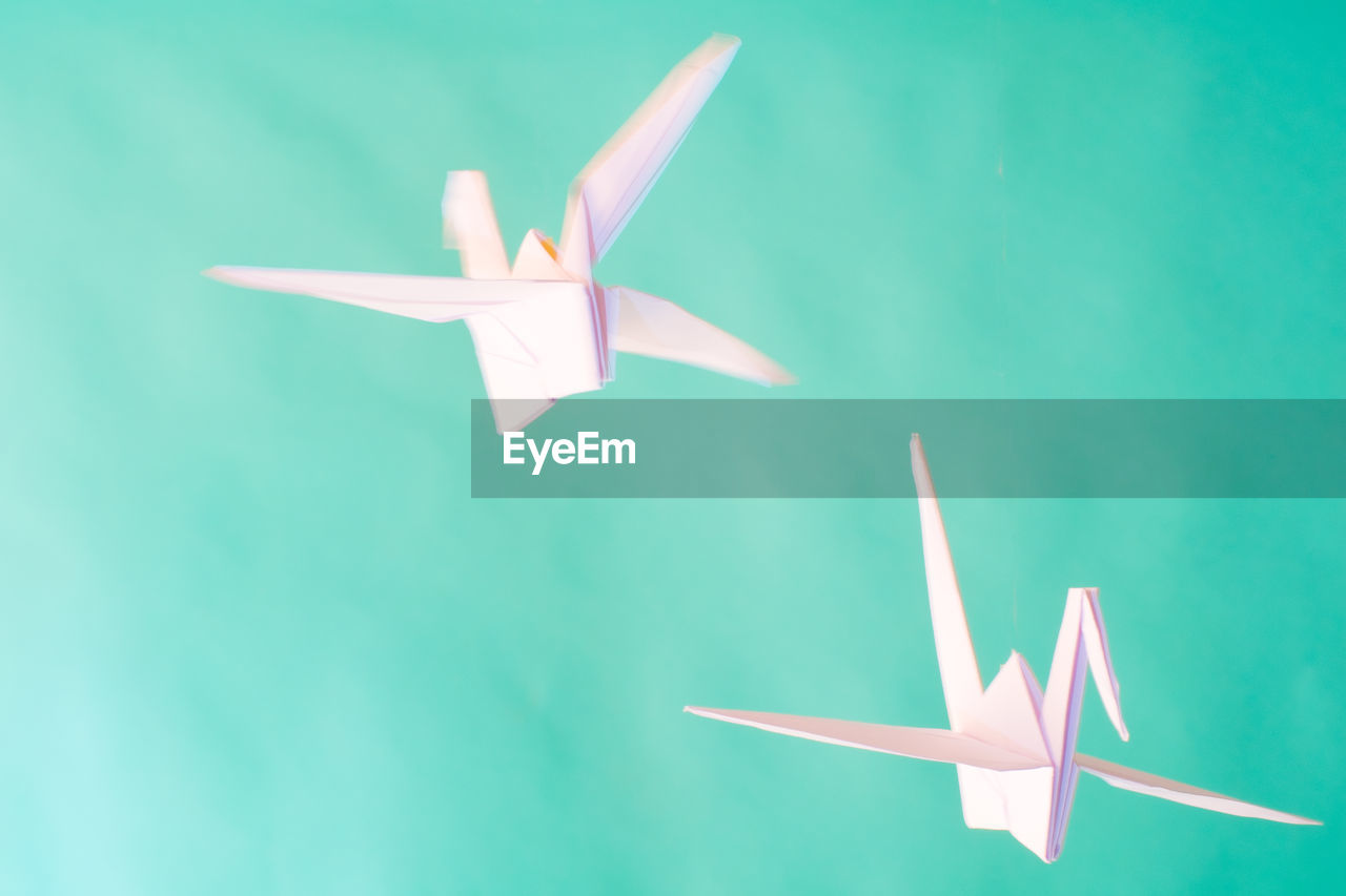 Origami cranes in mid-air against turquoise background