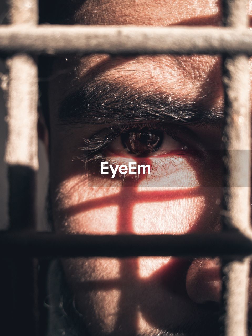 Close-up portrait of young man looking through metal grate