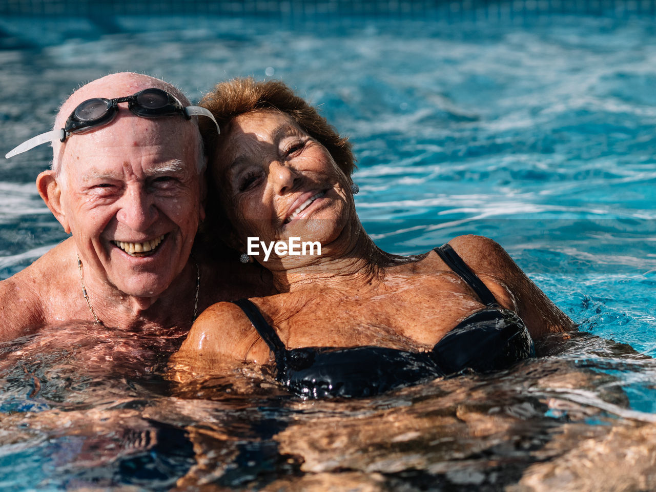 Cheerful senior couple smiling brightly while swimming together in outdoor pool during summer holidays