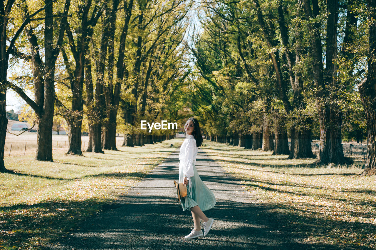 Portrait of woman standing on road amidst trees