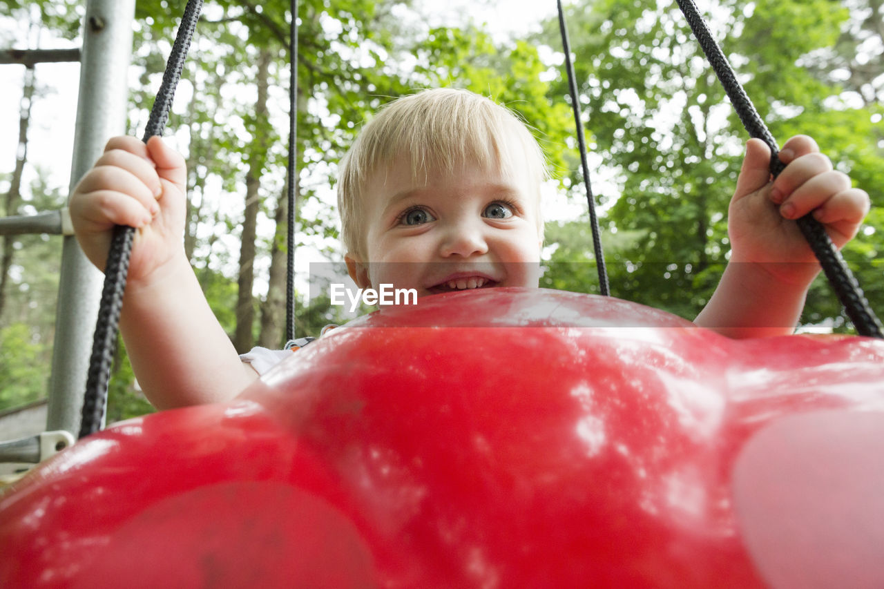 Cute baby boy swinging on red plastic swing at playground