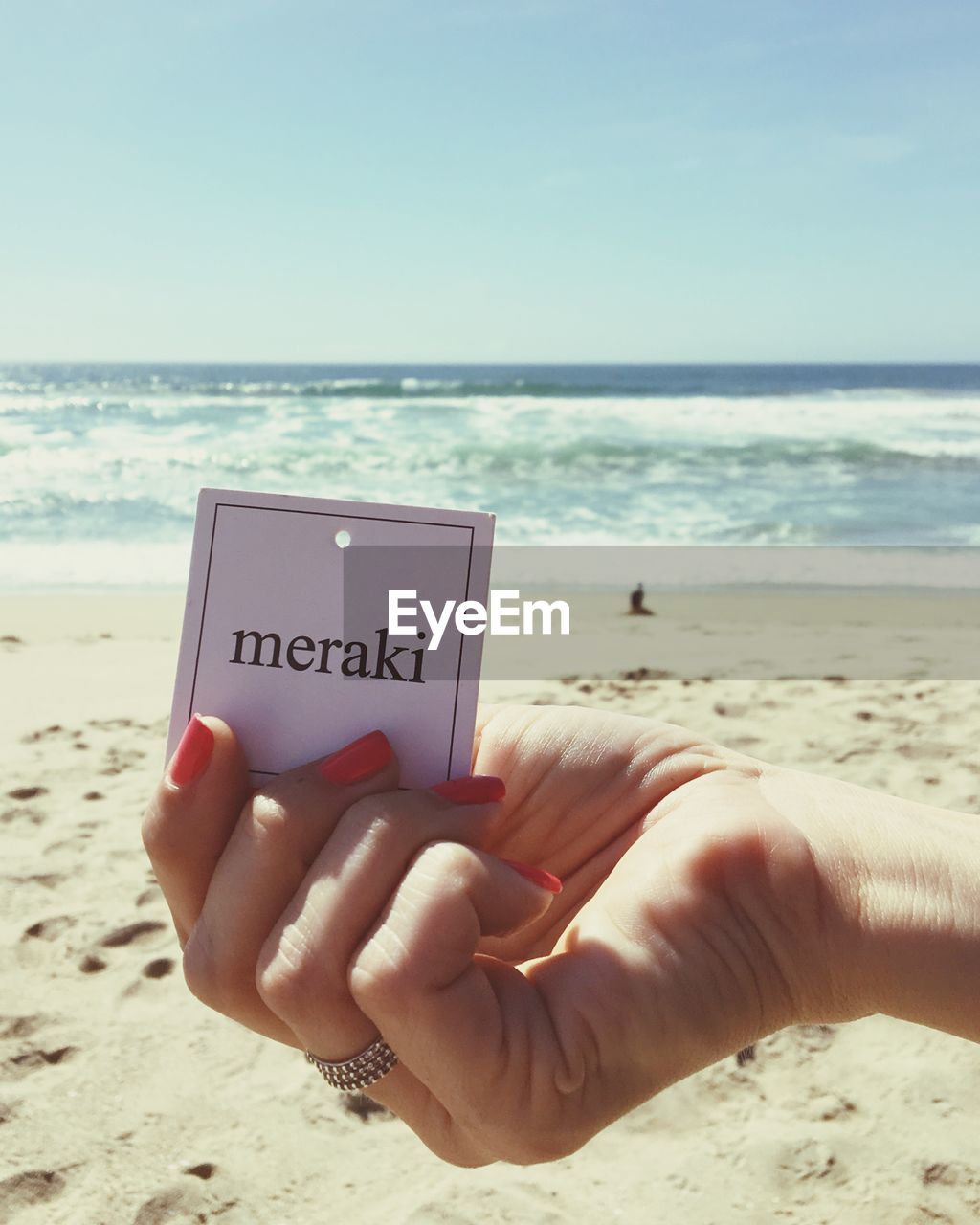 Cropped hand of woman holding meraki text at beach
