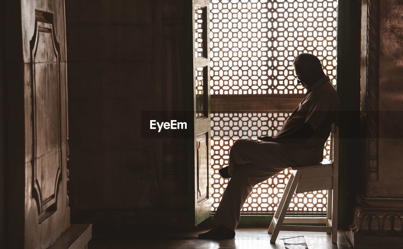 Side view of man sitting on chair against building
